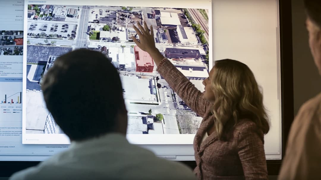 A woman gestures to an image of commercial real estate properties on a large monitor