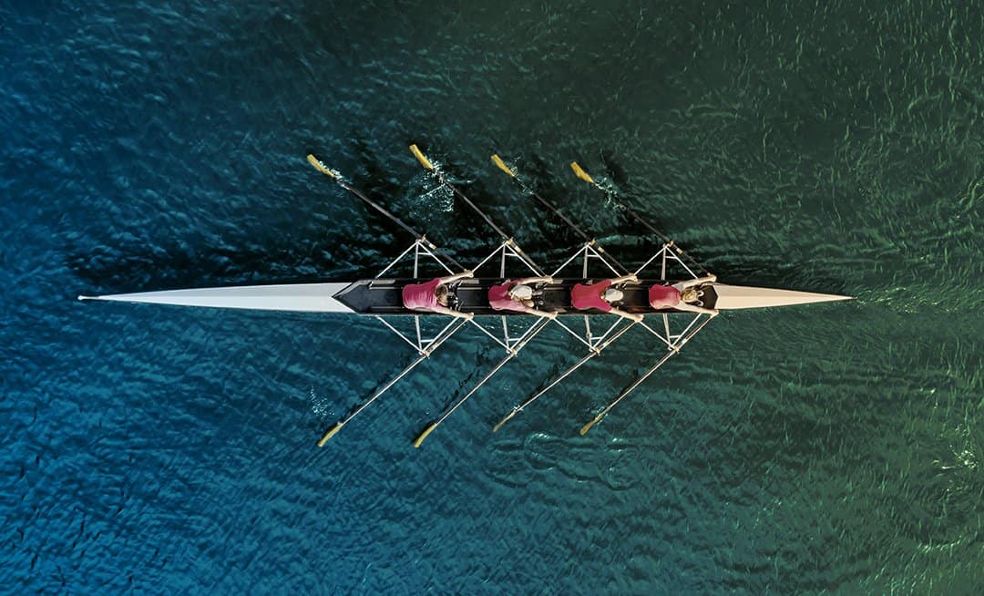 Overhead view of women's rowing team on blue water.