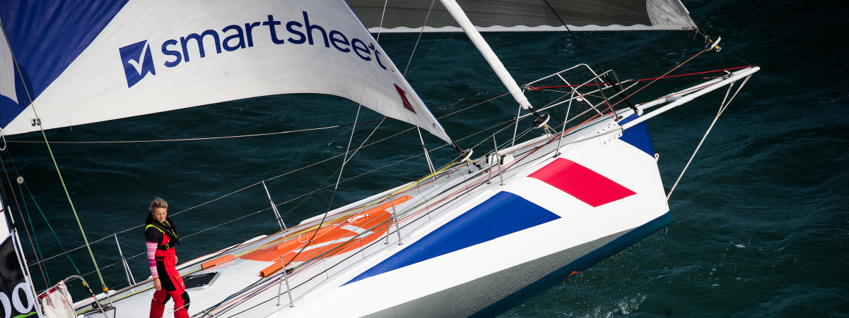 Pip Hare stands on board Medallia with the Smartsheet logo visible on the sail above her