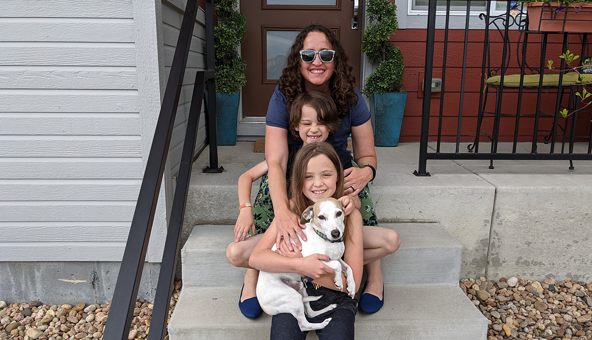 Tana sits on a stoop with her two children and a dog