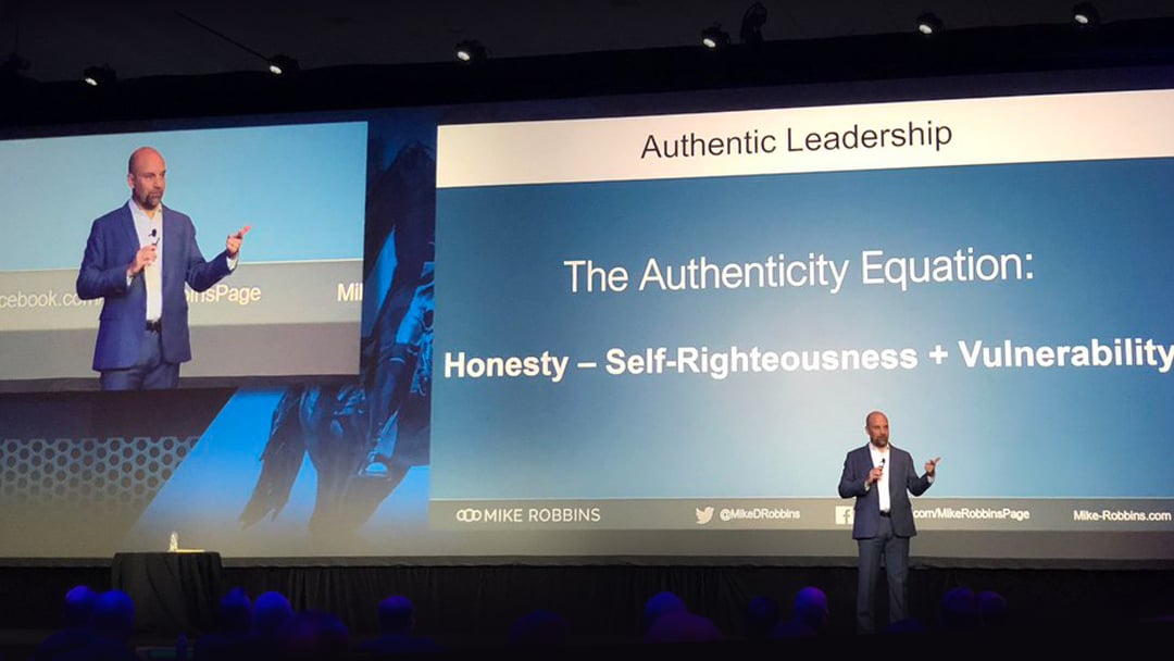 Mike Robbins delivers a keynote at a corporate event, presentation slide reads: "The Authenticity Equation: Honesty - Self-Righteousness + Vulnerability"