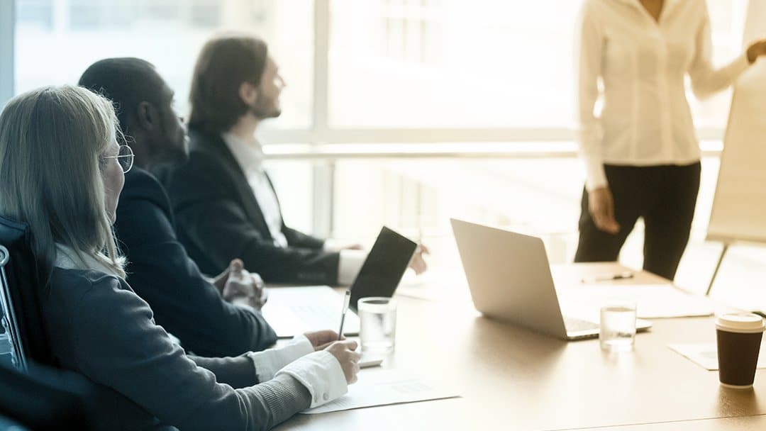 A woman presents to three business people in a conference room.